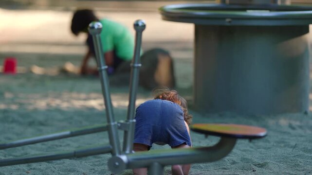 Toddler losing balance near playground digger then lowering to ground and transitioning into crawling capturing adaptability resilience and continued exploration in sandbox play