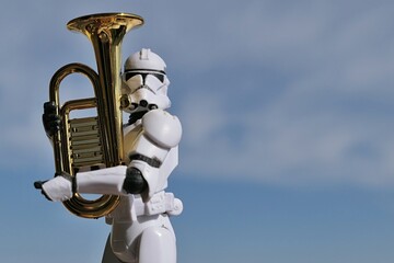 Naklejka premium Action figure of Star Wars clone trooper in white helmet and armor holding model of some kind of euphonium brass instrument, blue spring skies with overcast clouds in background. 