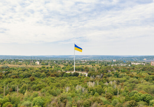 Large Ukrainian flag on a tall white flagpole over the green park in Kramatorsk city