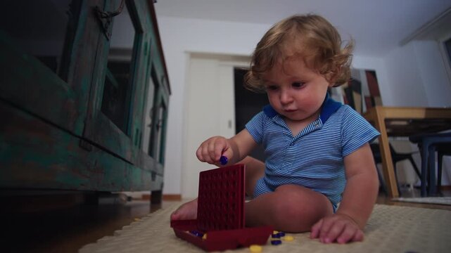Toddler smiling while placing colored token into grid board game while sitting on floor during playful learning moment at home, curiosity exploration and early development