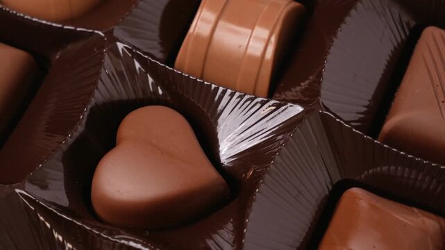 Appetizing chocolate candies of various shapes in stylish black corrugated packaging, rotating in a circle. Heart-shaped and chest-shaped candies.