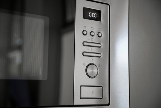 Close-up of a modern built-in microwave oven control panel. Brushed stainless steel finish with digital timer display, buttons, and a rotary knob. Sleek minimalist kitchen appliance design.