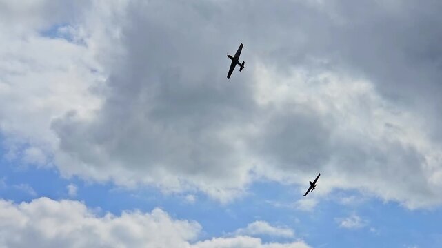 Pair of vintage propeller warbirds performing tactical maneuvers and aerial combat simulation in a cloudy sky.
