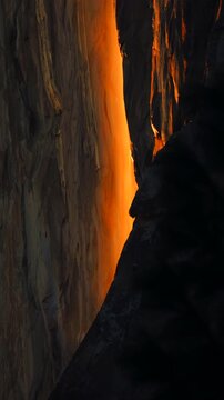 Vertical Screen: Yosemite National Park Firefall phenomenon with golden orange light illuminating Horsetail Fall on El Capitan granite cliff during February sunset with dark shadows
