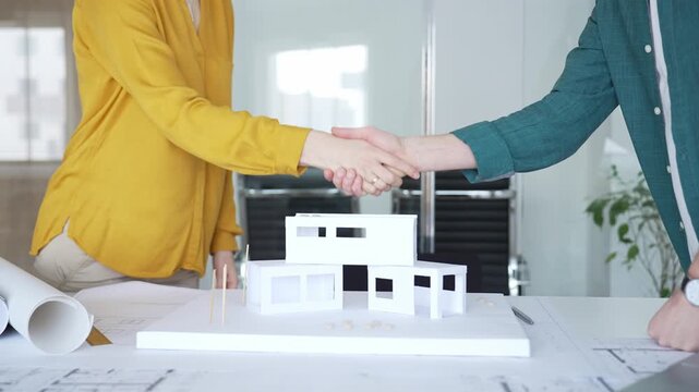Business partners shaking hands over architectural model, finalizing real estate deal during office meeting. Architecture and business concept