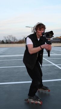 Vertical screen young videographer moving forward on roller skates holding camera on stabilizer carefully filming scene maintaining balance and smooth motion during outdoor video production