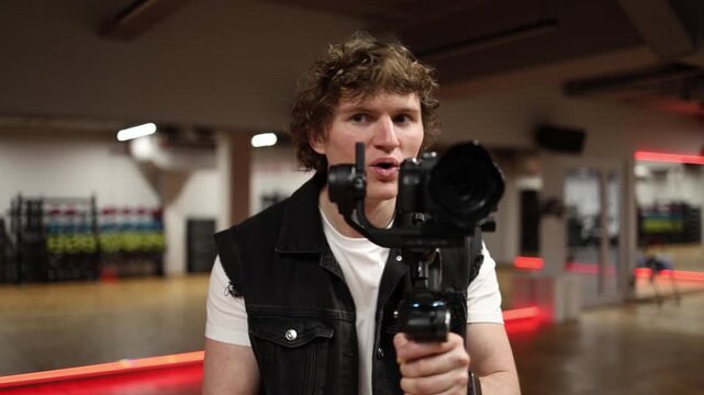 Cameraman holding camera on gimbal looks forward with open mouth showing strong positive reaction impressed by filming result and satisfied with captured footage