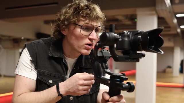 Young videographer strains eyes while adjusting camera on stabilizer in studio fatigue from long filming sessions overwork vision discomfort during content production