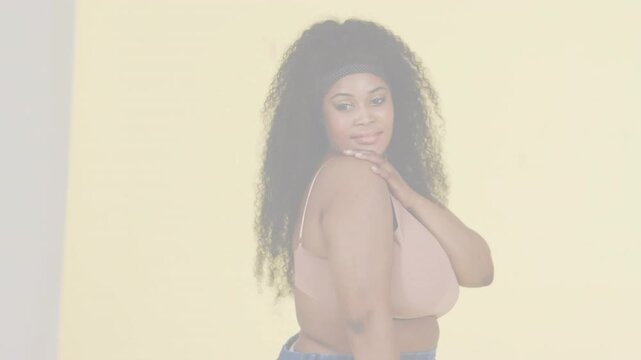 Model posing fashion shoot hand on shoulder as camera rolling pale yellow wall with faint streaks