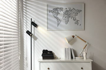 Stylish lamps, books, decor and chest of drawers near white wall indoors