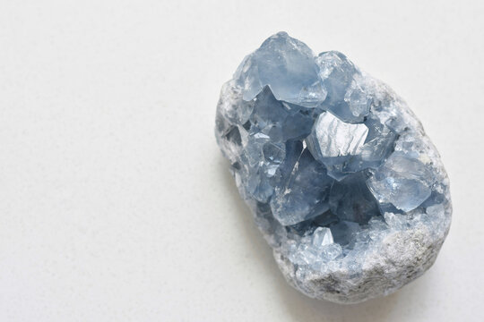 High-quality image of a natural celestite geode crystal resting on a clean white table. This blue celestine mineral features delicate sparkling formations and soft pastel tones