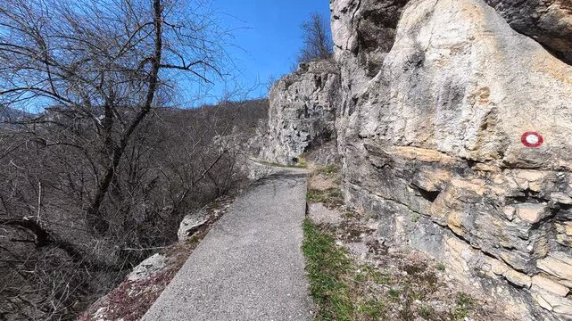 Path hugs steep cliffside under clear blue sky. Balkan, Eastern Europe, POV