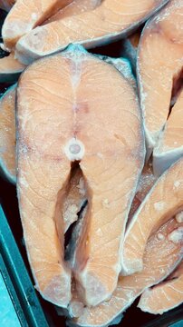 Fresh trout steaks on chilled shelf display, market presentation with ice crystals and glistening orange fillets, retail pricing.