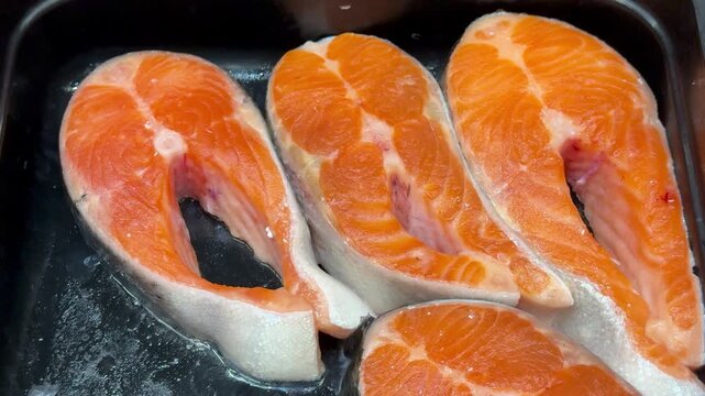 Fresh trout steaks on chilled shelf display, market presentation with ice crystals and glistening orange fillets, retail pricing.