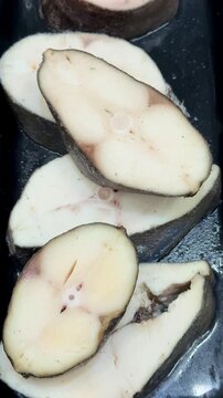 Butterfish steaks raw on black tray closeup of thick pale steaks with dark skin edge, moist sheen, subtle salt crystals, stainless.