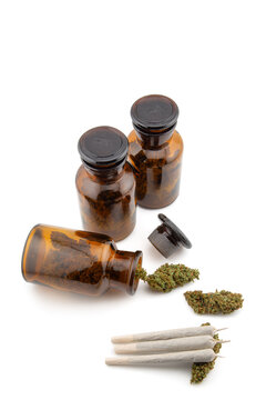 Professional Medical Cannabis Still Life with Dried Buds and Pre-rolled Joints in Amber Apothecary Glass Jars on White Background
