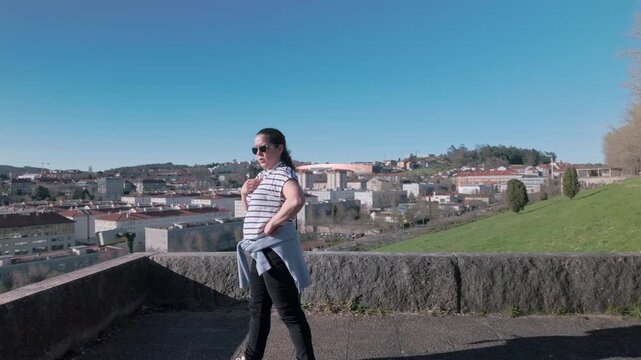 a middle age woman recovering after exercises and checking heart rate on a sunny day at a scenic viewpoint overlooking the city of Santiago de Compostela, enjoying a moment of freedom and happiness