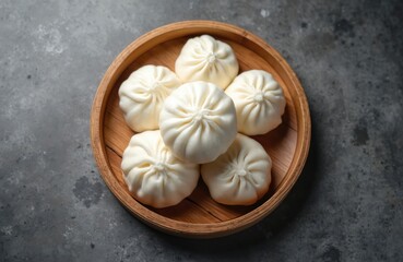 Fototapeta premium Steamed white baozi buns are served in a wooden steamer basket on a textured dark surface. These soft, fluffy dumplings are a popular Asian street food staple.