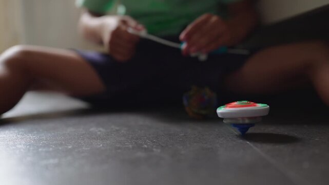 Spinning top toy rotating on floor in foreground while child prepares launcher in background playful childhood moment of motion focus and traditional toy play at home
