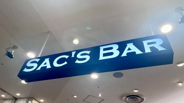 Sac's Bar retail store signage near a Starbucks cafe at Narita International Airport featuring modern blue branding and white illuminated text - Chiba, Japan, October 29, 2025