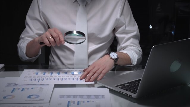 Businessman studying financial report data with magnifying glass, conducting detailed audit and analysis. Audit and taxes in business
