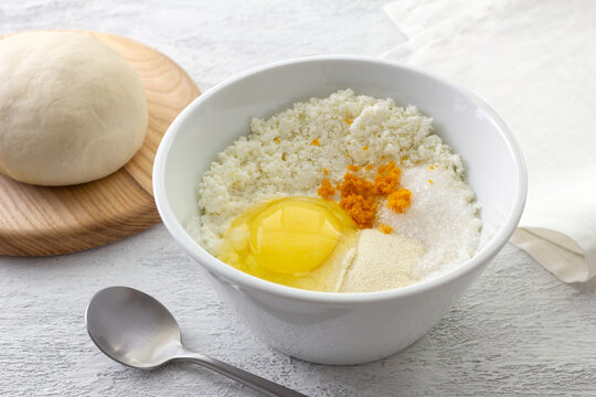 Ingredients for ricotta cheese filling in white bowl with raw egg orange zest semolina and sugar on kitchen table