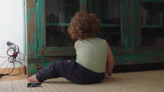 Toddler sitting on floor opening and closing cabinet door repeatedly curious childhood moment of cause and effect learning and playful interaction with household furniture at home