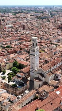 Aerial drone view of Verona's historic city center surrounded by the curved Adige River. The Verona Cathedral bell tower rises above red rooftops and historic architecture. Vertical