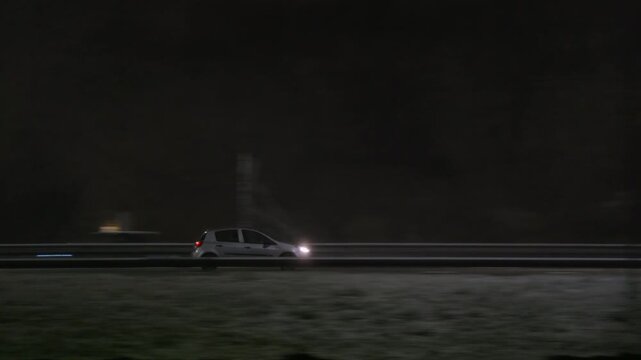 Side view pan of a hatchback driving on a highway under artificial lighting at night