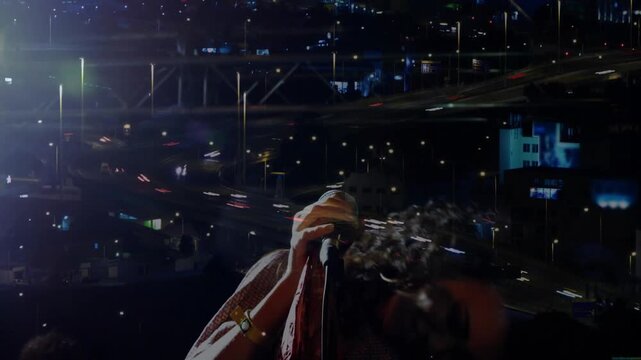 Singer starting singing on mic, leaning, whipping, raising arm, city streaking over her for music