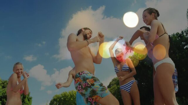 Man in floral trunks starting dance for leisure, group clapping, cheering amid lens flare bokeh