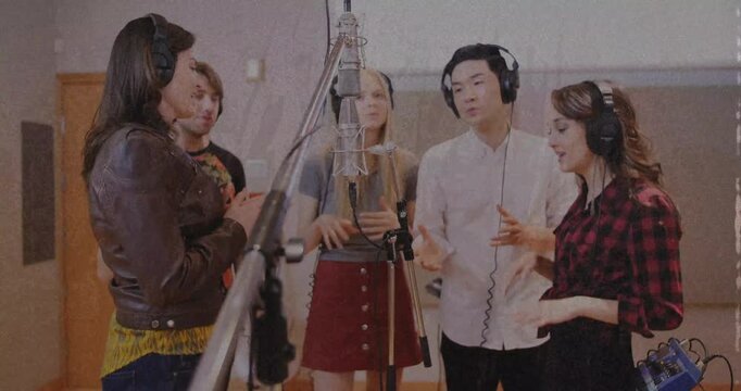 Five singers gathering round mic, white-shirt singer cuing hands, group harmonizing for recording