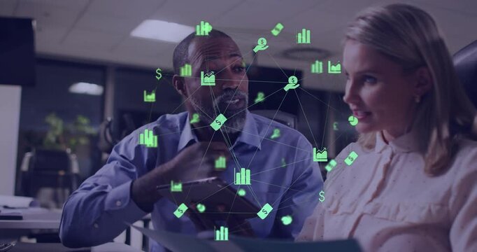 Man pointing sparking green data icons, woman reading papers, tapping tablet and reviewing finance