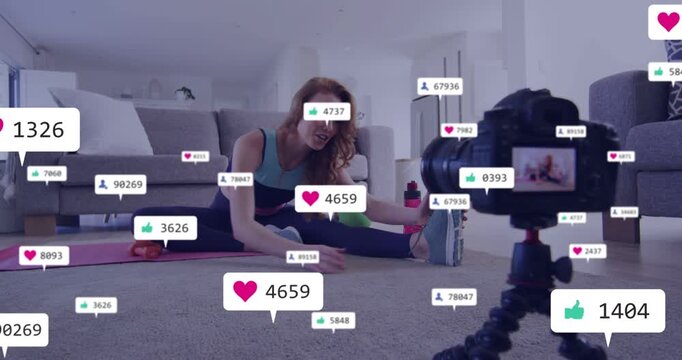 Woman fitness creator holding phone speaking to camera reaching toes as DSLR showing gaining likes