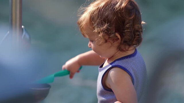 Toddler smiling while holding small shovel in sandbox capturing joyful curiosity playful engagement and outdoor childhood exploration in relaxed park environment