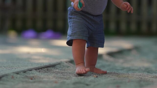Toddler stepping away from sandbox edge and walking forward through sand with small steady steps capturing balance development and confident outdoor childhood movement