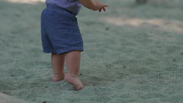 Toddler stepping barefoot into sandbox taking small steps before stumbling and sitting down capturing balance learning resilience and natural outdoor childhood exploration moment