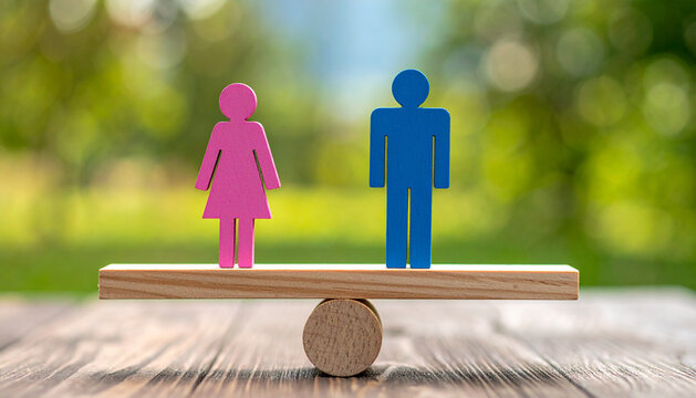 Pink and blue figurines on wooden seesaw symbolizing gender equality and balance.