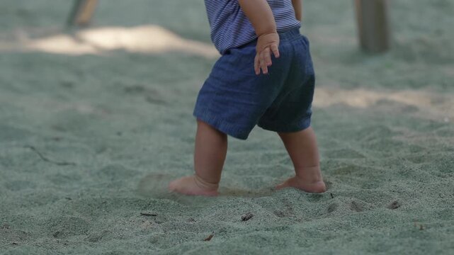Toddler walking forward in sandbox with energy then stumbling and falling again capturing persistence resilience and early balance development during outdoor childhood exploration
