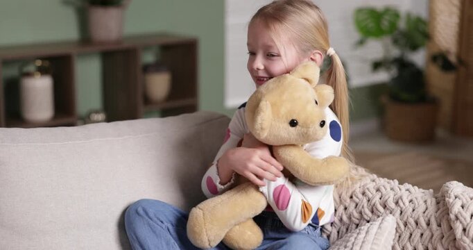 Little girl hugging her teddy bear on sofa at home