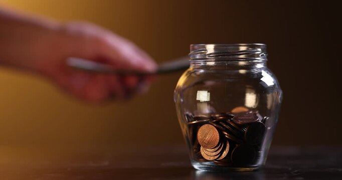 Woman putting banknotes near glass jar with coins at wooden table, closeup