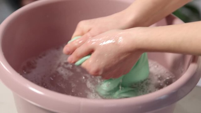 Woman washing stained kid's shirt in basinet at home, closeup