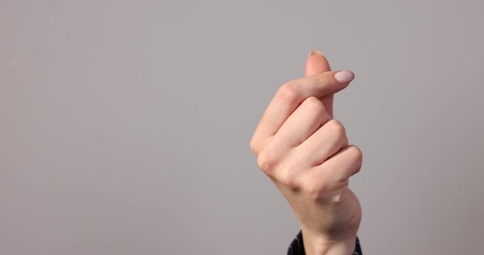 Woman showing heart gesture with fingers on light grey background, closeup