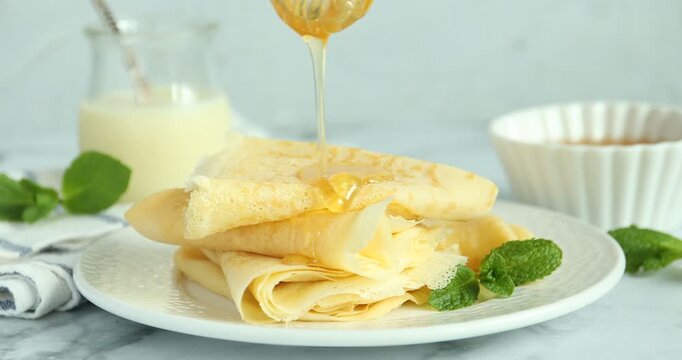 Woman dripping honey onto tasty crepes at white marble table, closeup