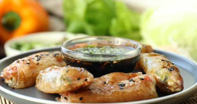 Plate with delicious fried spring rolls wrapped in rice paper and soy sauce turning against blurred background, closeup