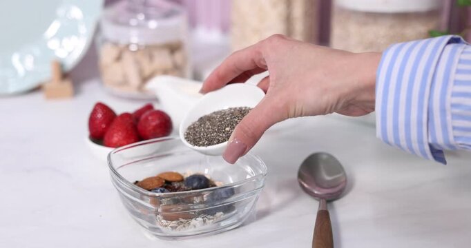 Oatmeal for breakfast. Woman adding chia seeds to mix and pouring it with milk, closeup
