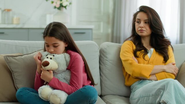 Offended Caucasian mother sister angry looking at sad upset little girl child woman female kid daughter hugging teddy bear mom indoors at home problem family quarrel conflict abuse misunderstanding