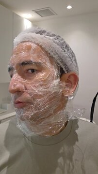 Treatment, cure of face skin in dermatology clinic. Scars procedure with problem skin for man. Man with cream with anesthesia and plastic film on his face before laser therapy procedure.