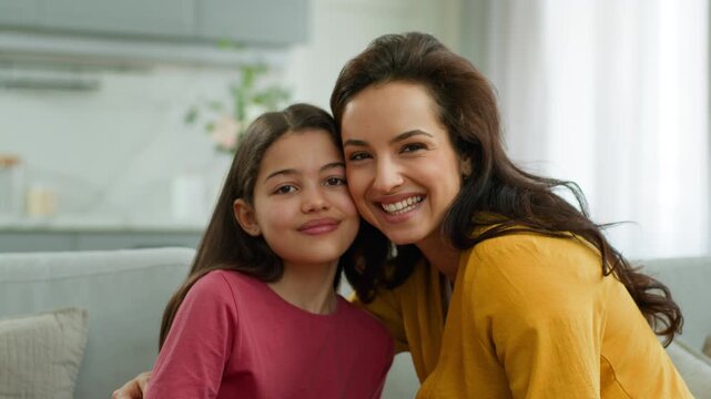 Happy family Caucasian woman mom touching forehead hugging little girl daughter love bonding female mother cuddling preschool child kid on sofa embracing hug motherhood relationship at home parenting