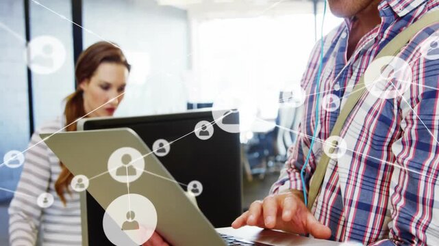Man holding laptop typing and sparking network icons in tech office, donning headphones connecting